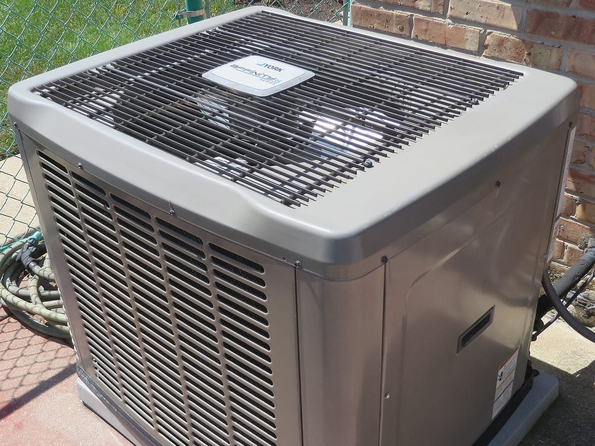 A central air conditioner condenser beside a brick house