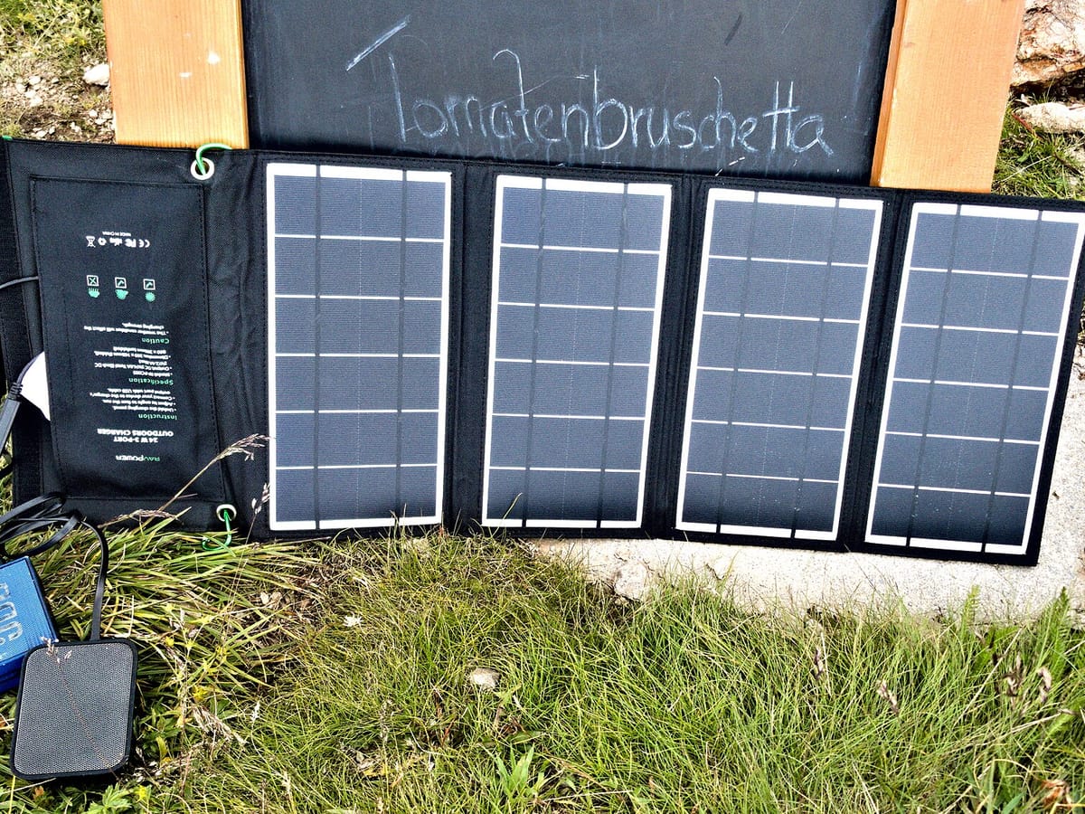 A folding solar panel charging a battery pack on grass